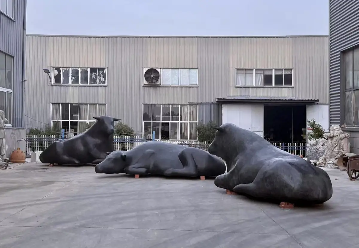 Three large black bull sculptures resting at the foundry yard