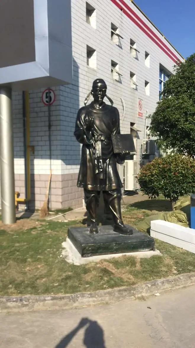 Bronze figure in traditional robes standing outdoors on a plinth