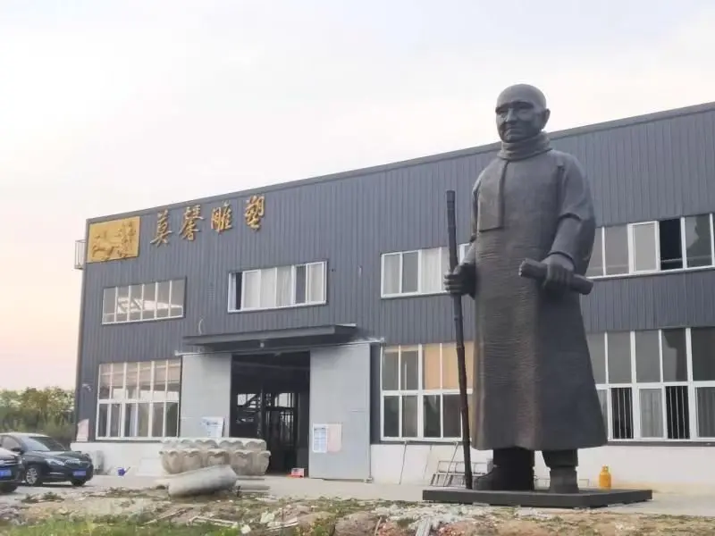 Large bronze figure in robe holding a staff outside the foundry