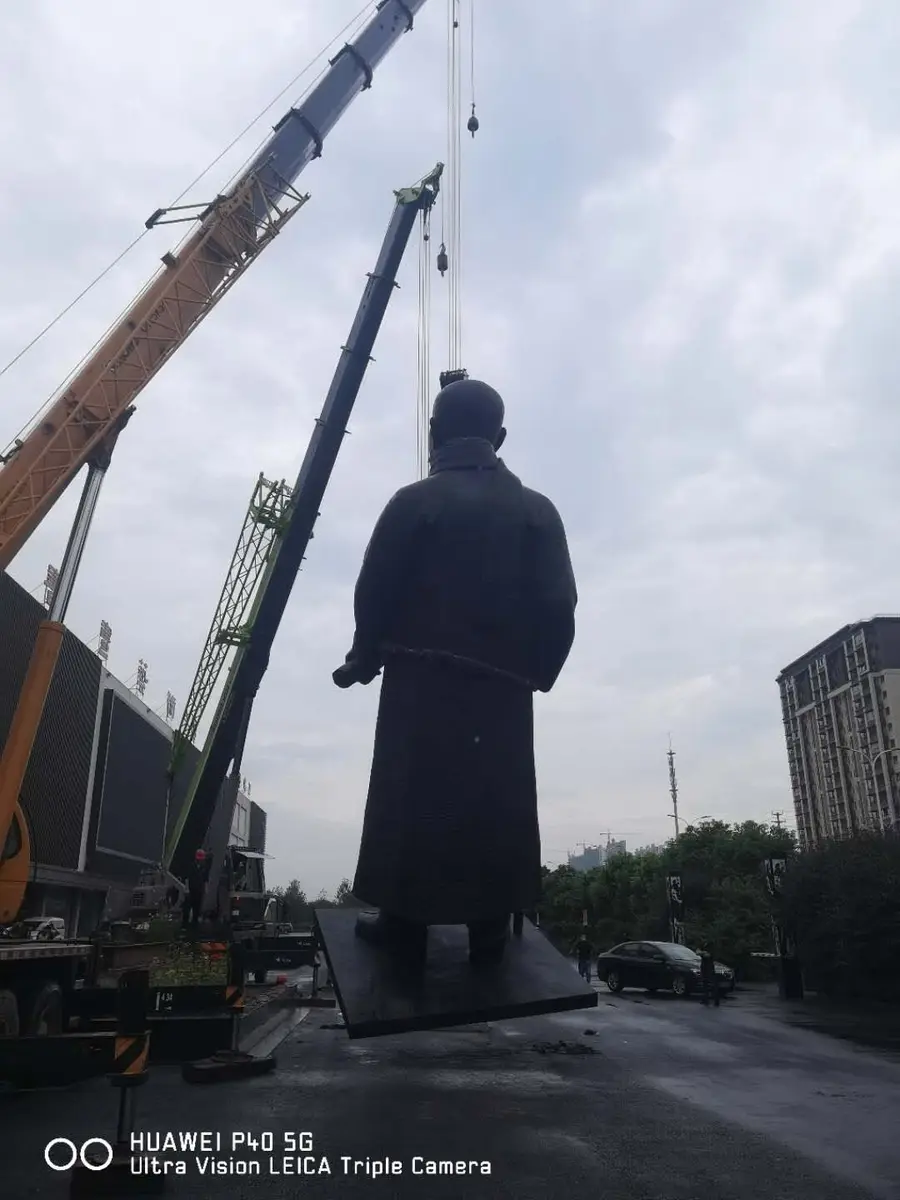 Bronze statue being lifted into place by cranes