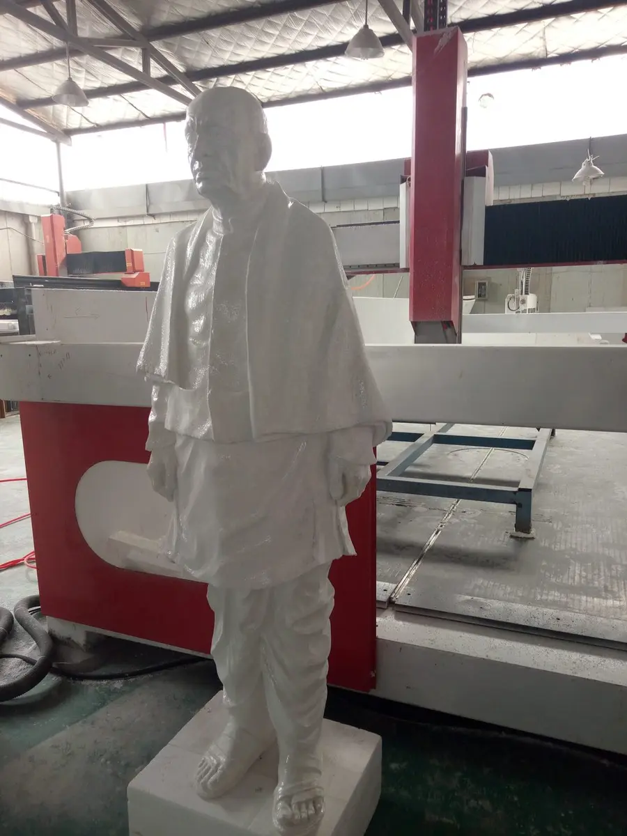 White figure sculpture beside a large CNC carving machine