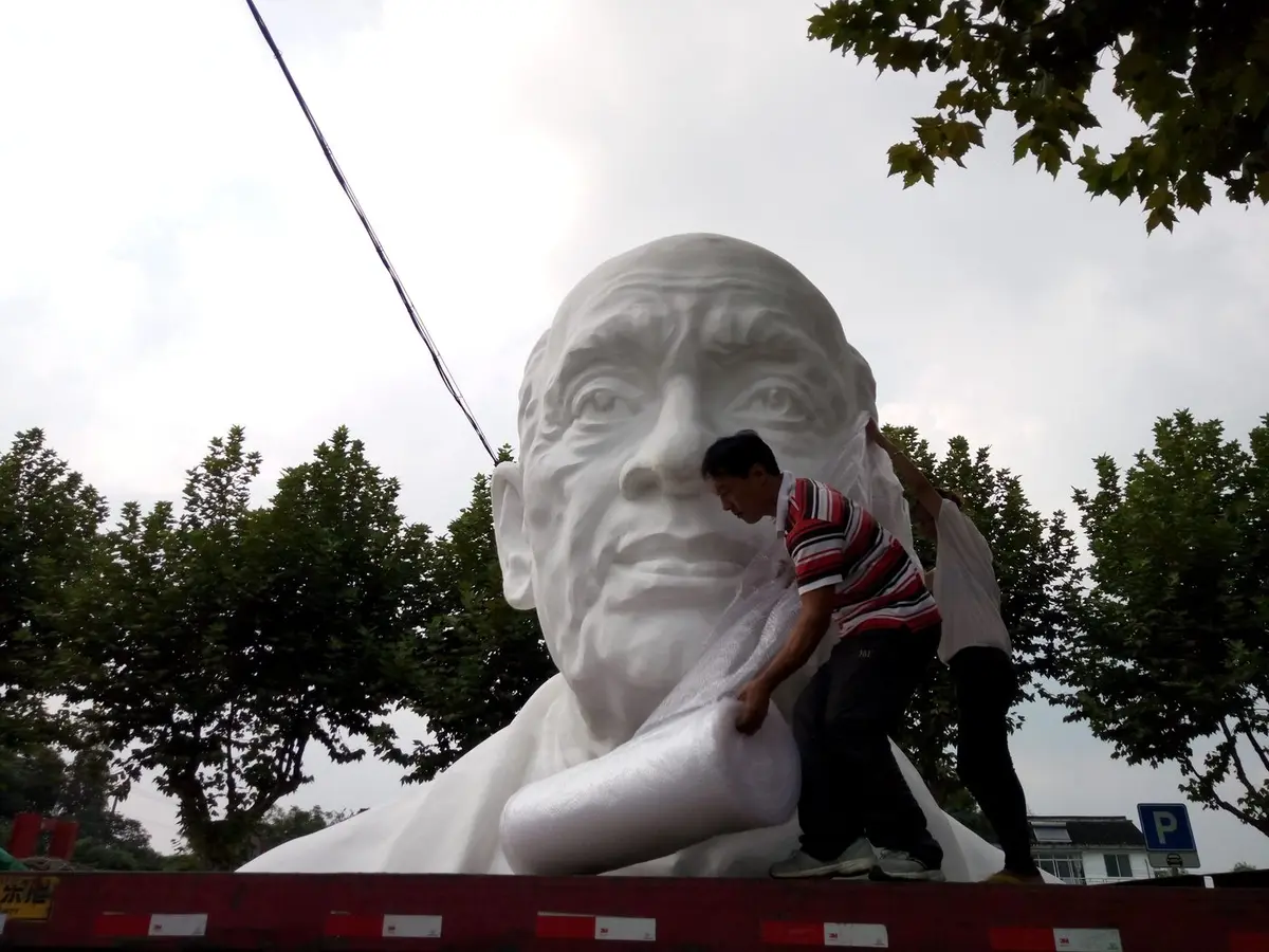 Workers wrapping a large white figure sculpture for transport