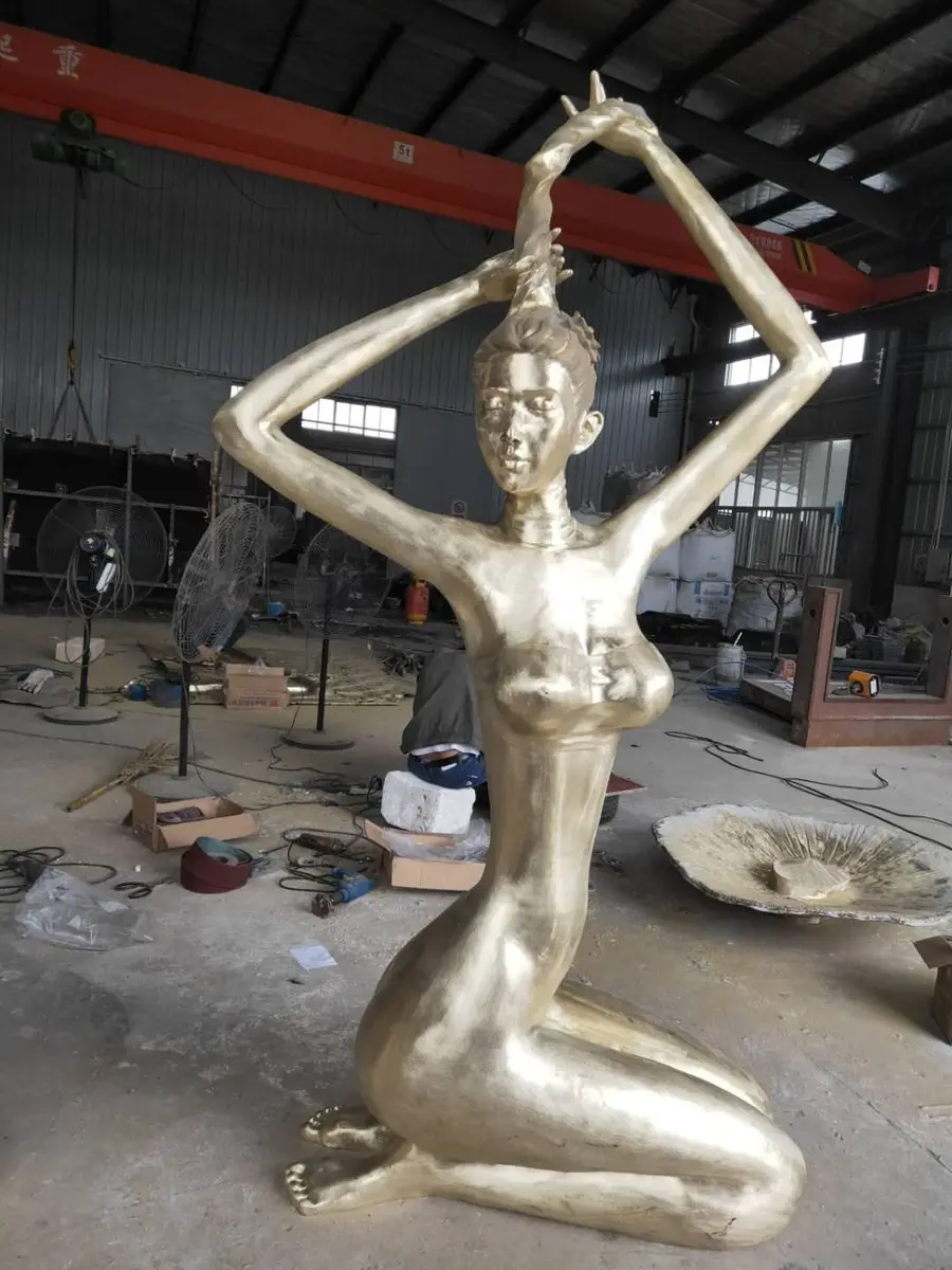 Golden kneeling female figure with raised arms in the workshop