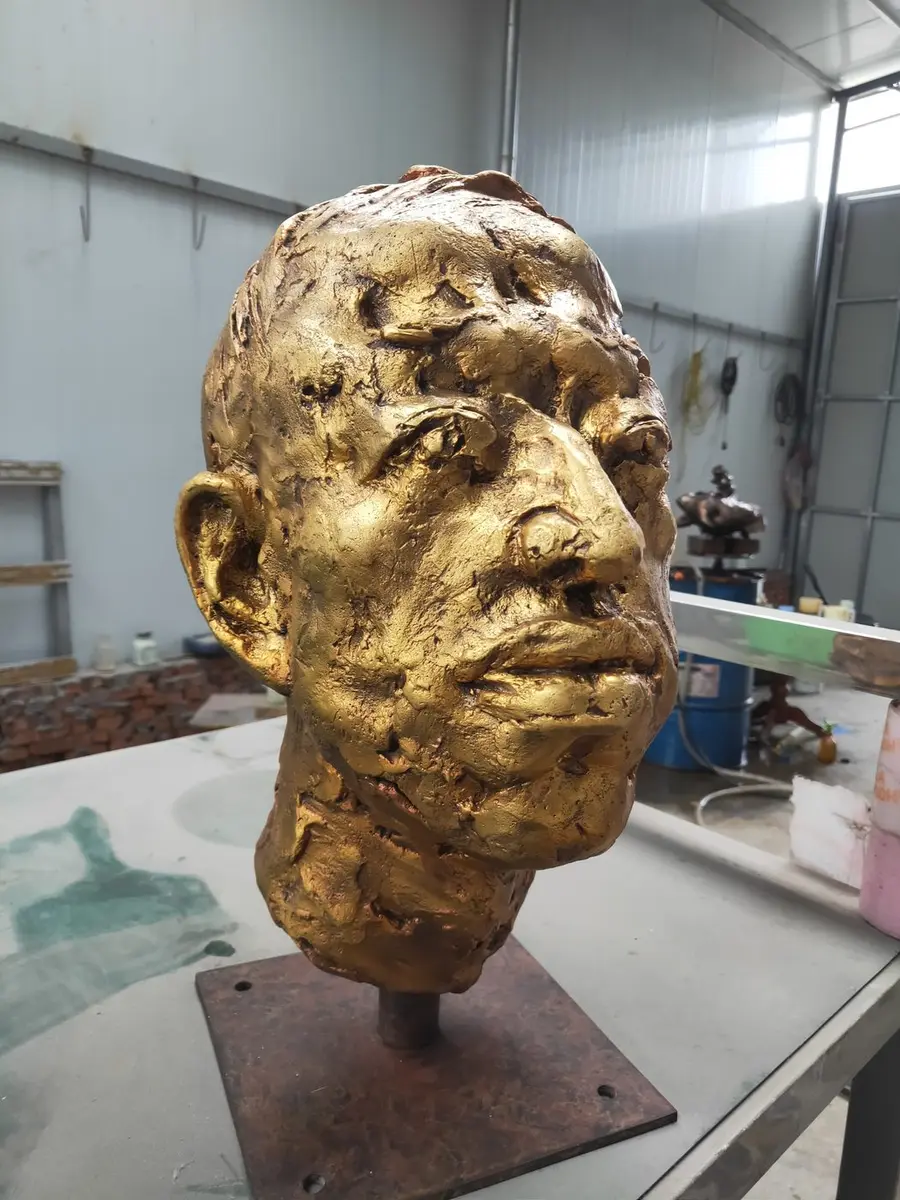 Golden portrait head sculpture with textured surface on a workbench