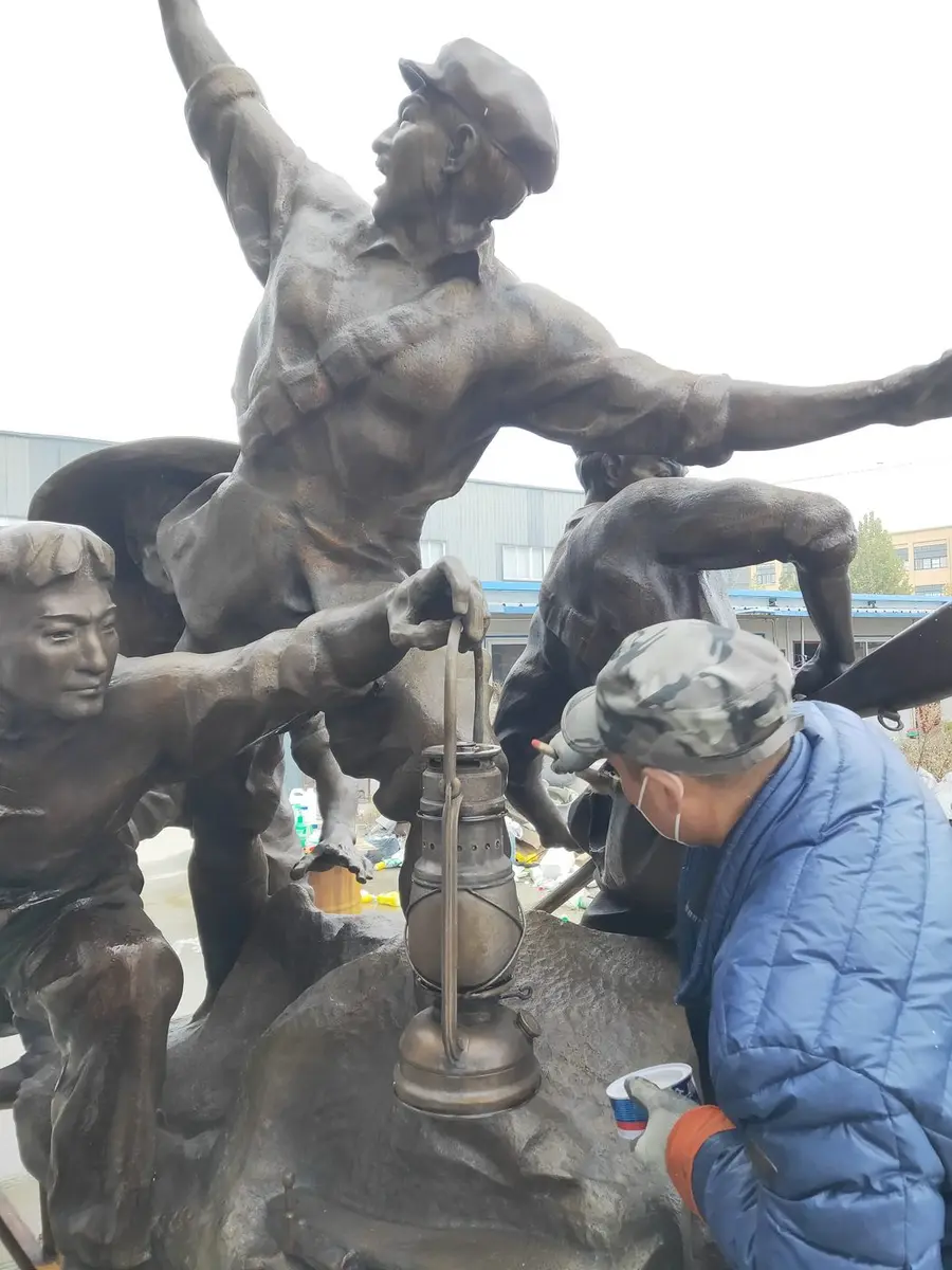 Worker applying surface paint to a monumental bronze group sculpture