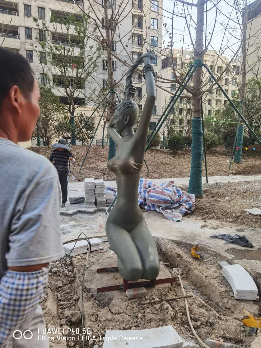 Kneeling bronze figure being installed in a landscape
