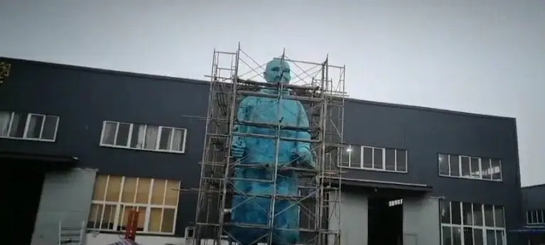 Large blue figure sculpture under scaffolding at the factory