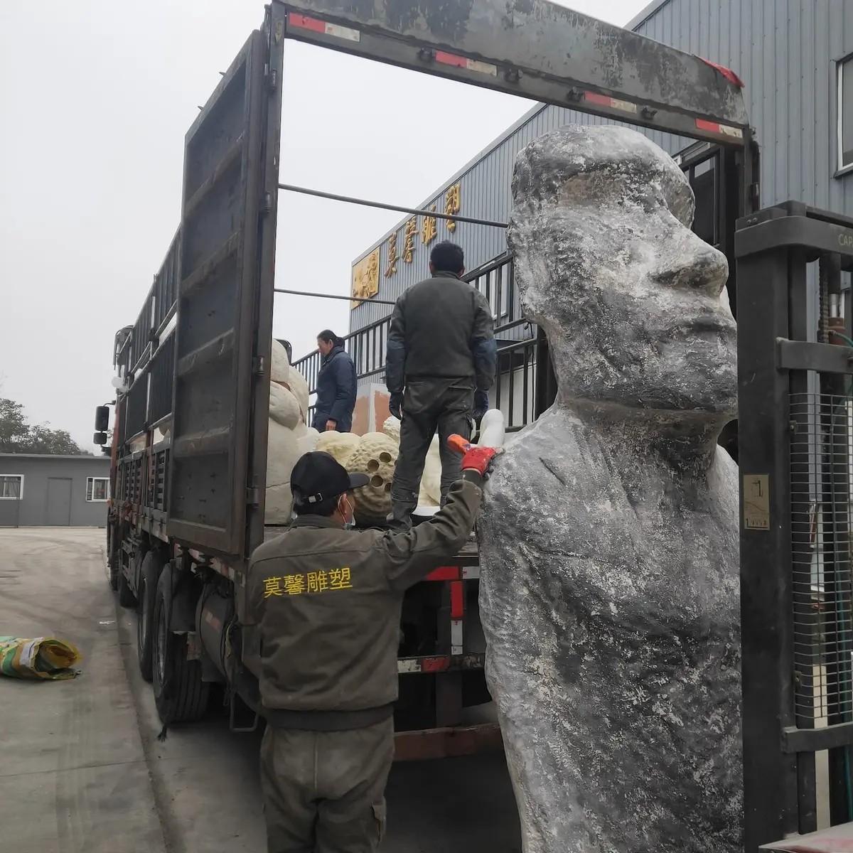 Workers loading a monumental bronze bust onto a truck