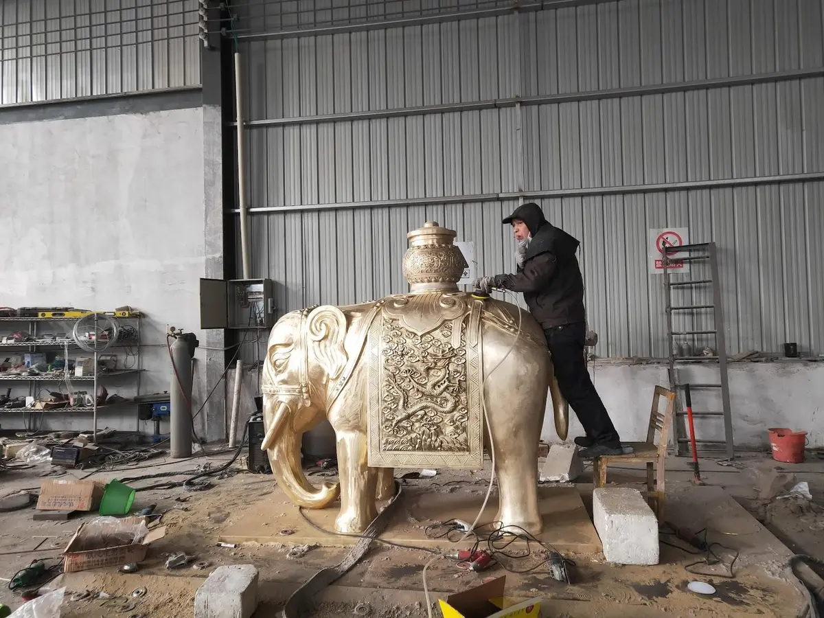 Craftsman polishing a golden elephant sculpture with dragon reliefs