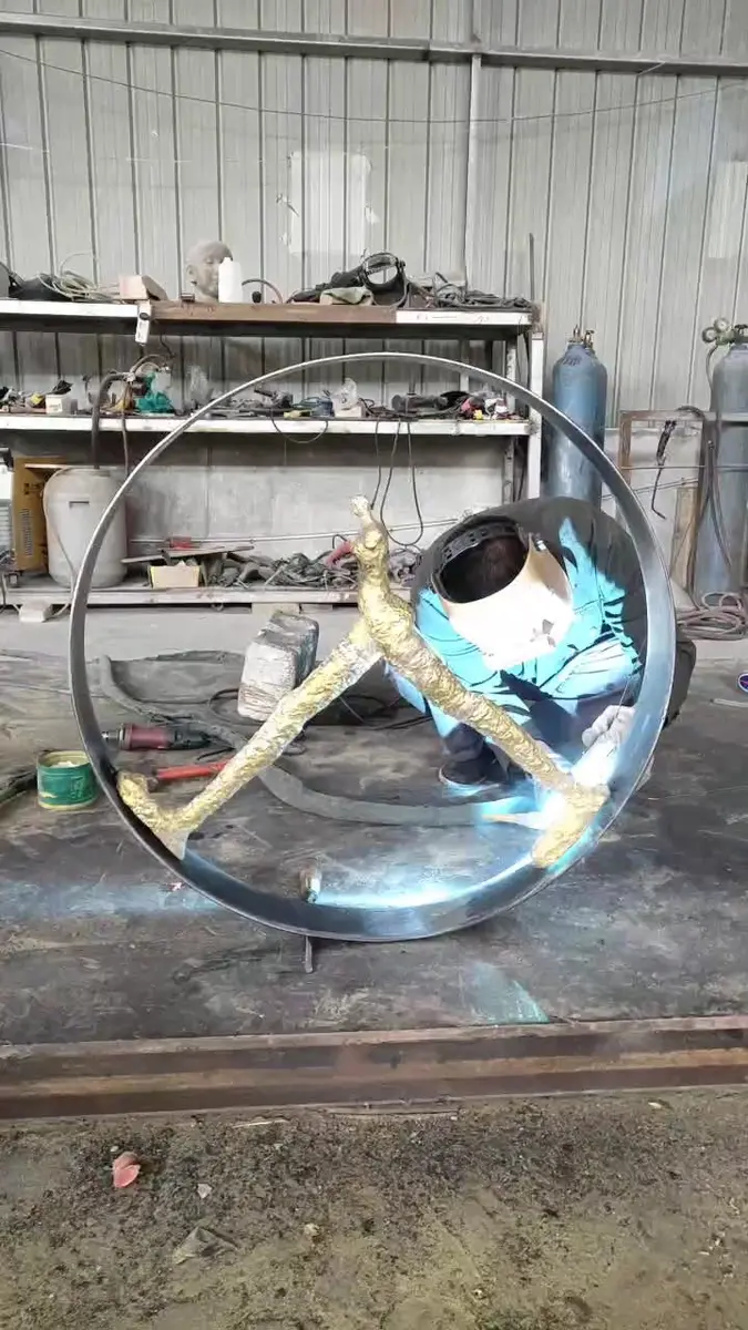 Welder working on a large metal ring sculpture with a golden figure inside