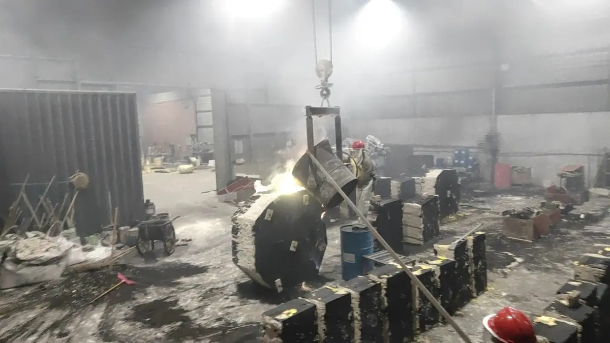 Molten metal pouring from a crane-hung vessel in the dark foundry