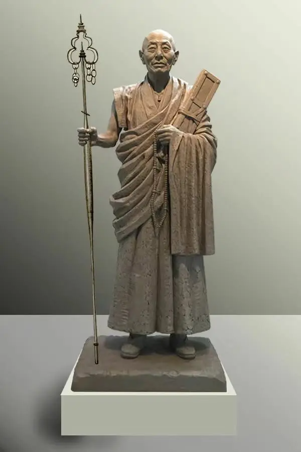 Bronze sculpture of a monk holding a staff and prayer beads