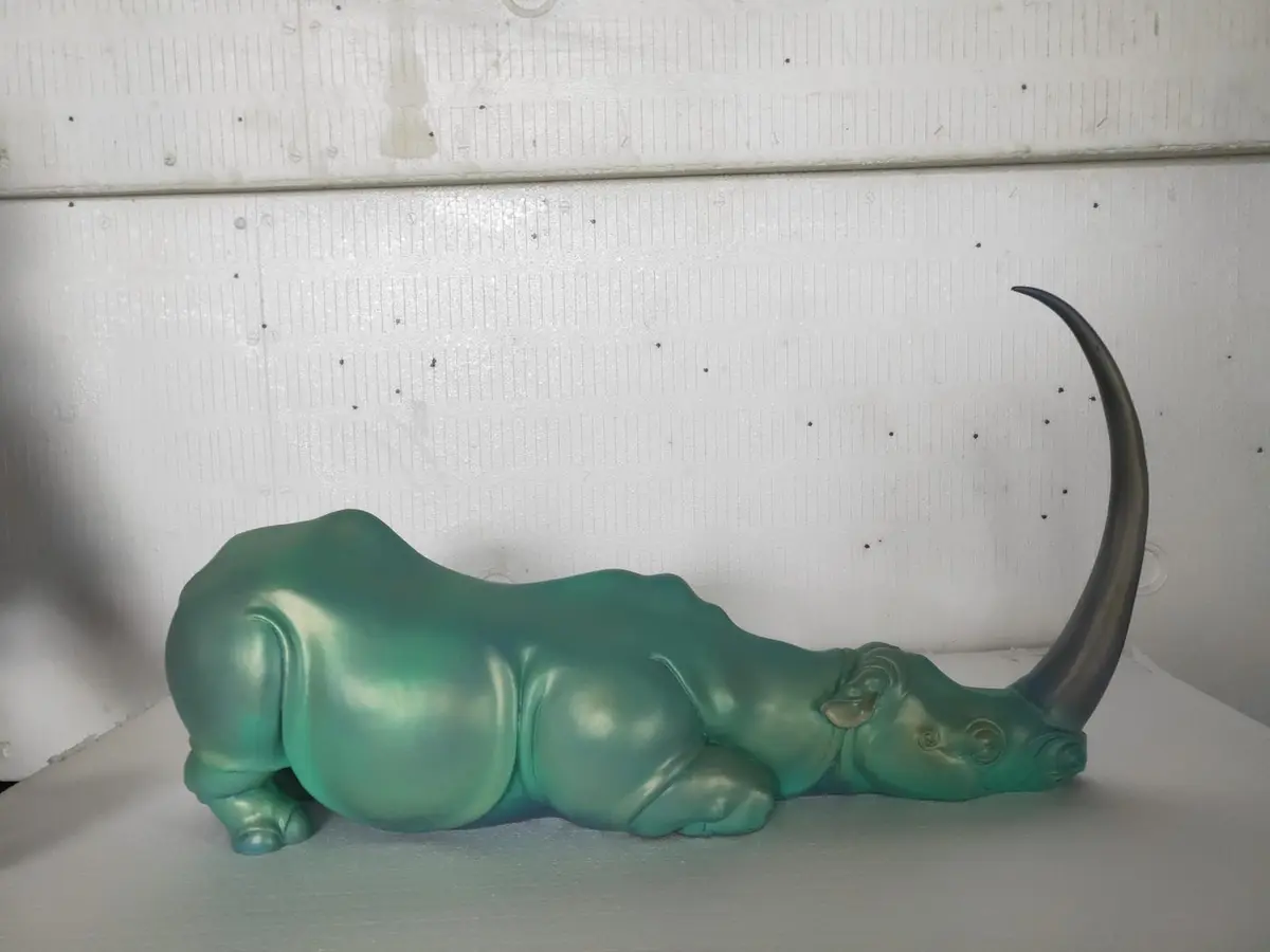 Pearl-finish rhino sculpture with green and blue iridescent patina